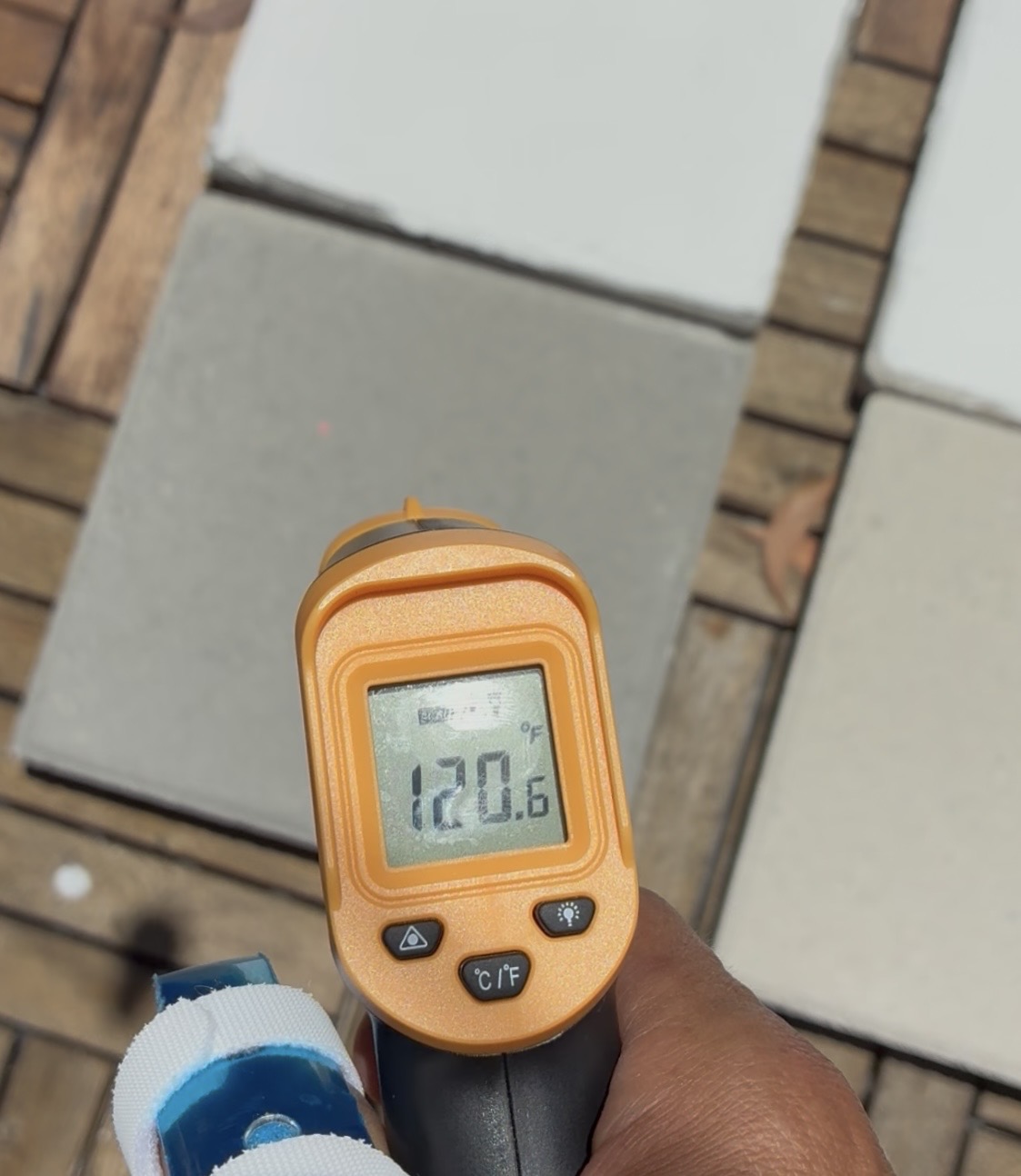 Infrared thermometer reading 120.6°F on an untreated control concrete panel in full sun